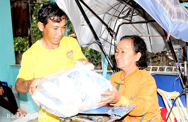 Bà Trần Thị Rằm nhận cơm từ thiện và di chuyển trên chiếc xe lăn để đưa cơm về cho người khuyết tật không di chuyển được