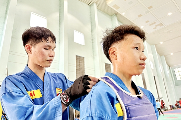 Em Nguyễn Hữu Tài (trái) giúp em ruột Nguyễn Đại Lộc đeo áo giáp trong các buổi tập - đây là cặp anh em ruột có thành tích tốt trong Đội năng khiếu vovinam của Trường phổ thông Năng khiếu thể thao Đồng Nai hiện nay