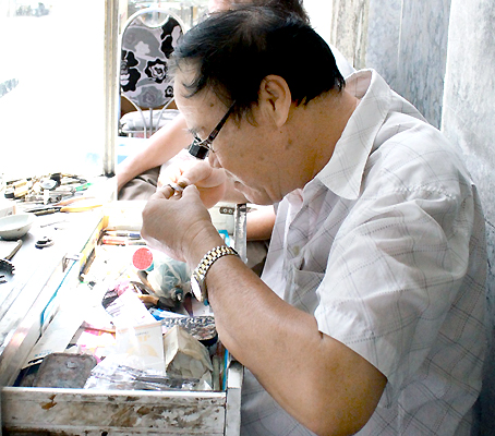 Ông Phạm Kiều Long với chiếc kính lúp quen thuộc ngày ngày vẫn ngồi bên góc đường Nguyễn Thị Hiền sửa đồng hồ cho khách.