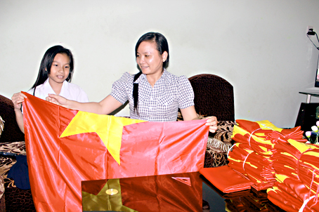 Bà Phạm Thị Anh (phải) đang dạy con gái gấp cờ để giao cho khách.
