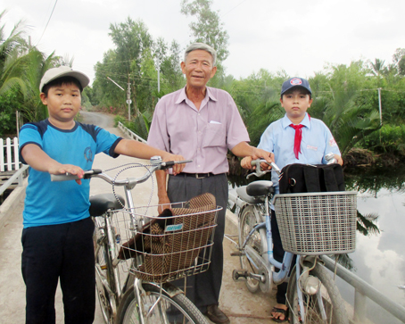 Ông Bảy Việt cùng học sinh bên cây cầu bê tông được làm từ sức dân.