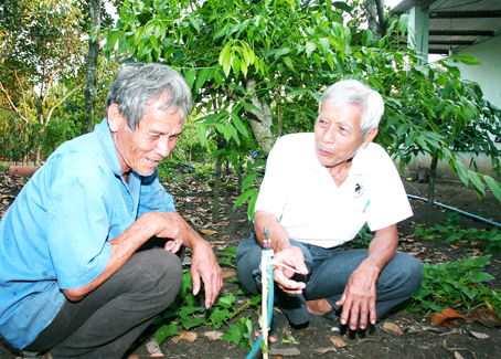 Ông Đinh Văn Phan (phải) trao đổi kinh nghiệm về sử dụng hệ thống tưới tự động với một nông dân trong ấp.
