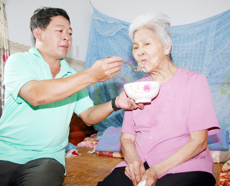 Bà mẹ Việt Nam anh hùng Nguyễn Thị Ký (86 tuổi, ngụ xã Nam Cát Tiên) được con trai nuôi Trần Văn Hòa chăm sóc từng bữa ăn.