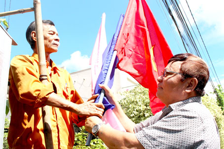 Ông Đặng Hữu Hoa (đứng trên thang gỗ) phấn khởi cùng ông Phạm Văn Dụng thử nghiệm giá treo cờ trên các cột điện do ông chế tạo.