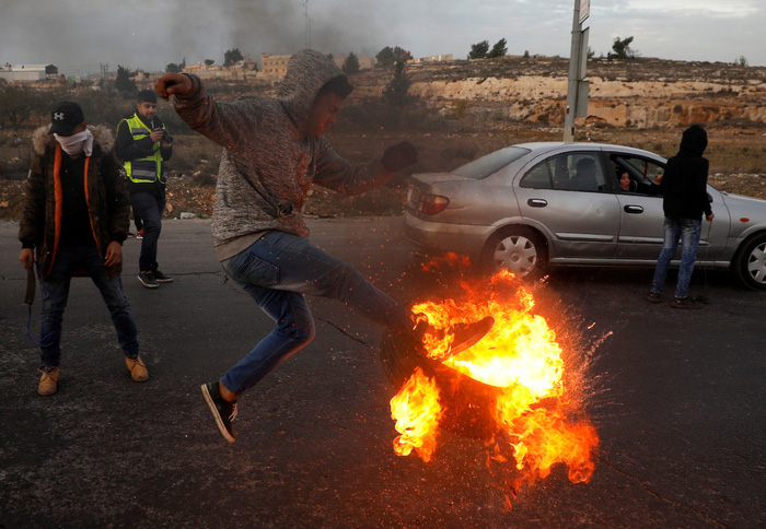 Người biểu tình Palestine đá một vỏ xe được châm lửa về phía binh sĩ Israel tại thành phố Ramallah, khu Bờ Tây ngày 10-12 - Ảnh: REUTERS