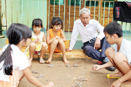 Già làng Nguyễn Văn Long xem các trẻ em dân tộc Chơro chơi ô quan.