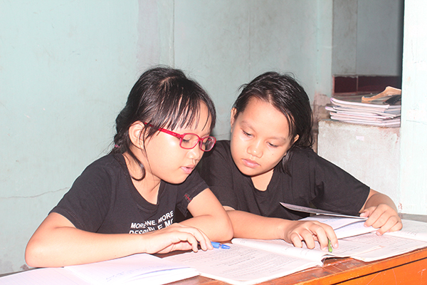 Em Nguyễn Thùy Trang (bìa trái) đang chỉ lại bài cho cô em gái song sinh Thùy Linh ở nhà vào buổi tối.