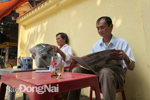 Phụ huynh ngồi đọc Báo Đồng Nai trong lúc chờ thí sinh dự thi trước điểm thi trường Sông Ngữ Lạc Hồng 