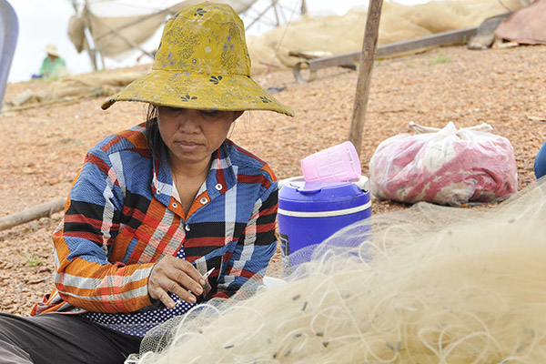 Bà Tám Vui (ngụ xã Mã Đà, huyện Vĩnh Cửu) đang vá lưới thuê cho các ngư dân