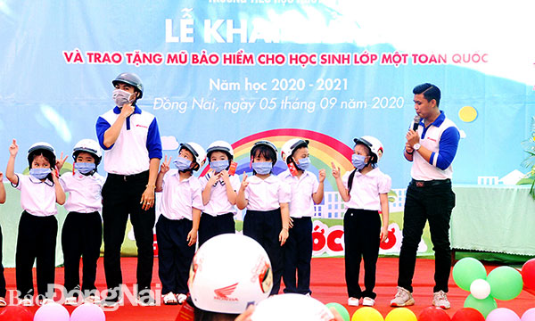 Nhân viên Công ty TNHH Honda Việt Nam hướng dẫn các em học sinh lớp 1 Trường tiểu học Nguyễn Du (TP.Biên Hòa) đội mũ bảo hiểm an toàn. Ảnh: T.Hải