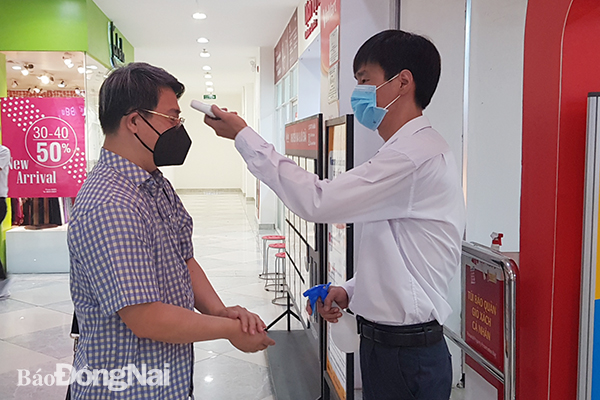 Nhân viên tại một trung tâm thương mại ở TP.Biên Hòa tiến hành kiểm tra thân nhiệt cho khách hàng. (Ảnh: Lam Phương)