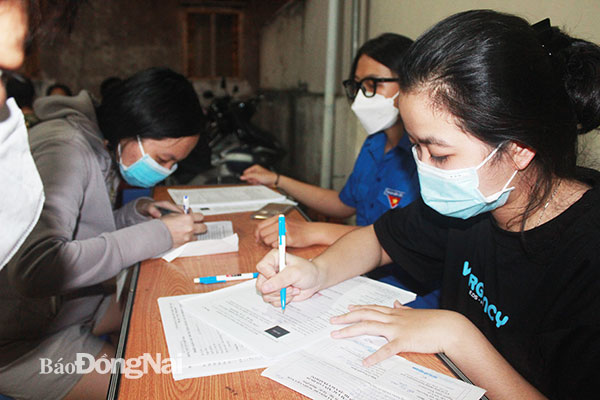 Tình nguyện viên ở TP.Biên Hòa hỗ trợ ghi chép thông tin cho người dân khi đến tiêm vaccine mũi 3 tại điểm tiêm lưu động vào buổi tối. Ảnh: Hạnh Dung