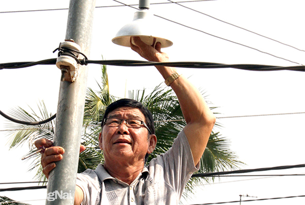 Ông Hoàng Văn Diệp, Trưởng ban Công tác Mặt trận ấp Thái Hòa, xã Phú Túc (H.Định Quán) thay bóng đèn bị hư hỏng ở một trụ đèn. Ảnh: S.Thao