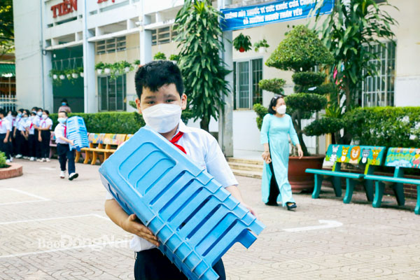 Học sinh Trường tiểu học Quang Vinh (P.Quang Vinh, TP.Biên Hòa) cất những chiếc ghế nhựa do phụ huynh mua sắm sau giờ sinh hoạt ngoài trời. Ảnh: Công Nghĩa