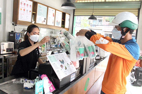 Shipper của một ứng dụng giao đồ ăn nhận đơn tại một cửa hàng nước uống trên đường Nguyễn Ái Quốc (TP.Biên Hòa) để giao cho khách. Ảnh: H.Lê