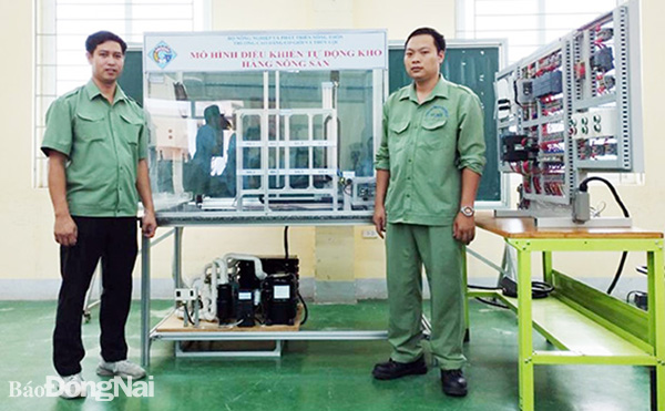 Thầy giáo Phạm Minh Phong, giảng viên Khoa Điện - điện tử, Trường cao đẳng Cơ giới và thủy lợi (bên trái) và đồng nghiệp bên mô hình điều khiển tự động kho hàng nông sản. Ảnh: H.Yến